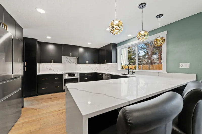 Sage green painted walls behind a quartz peninsula and gold pendants