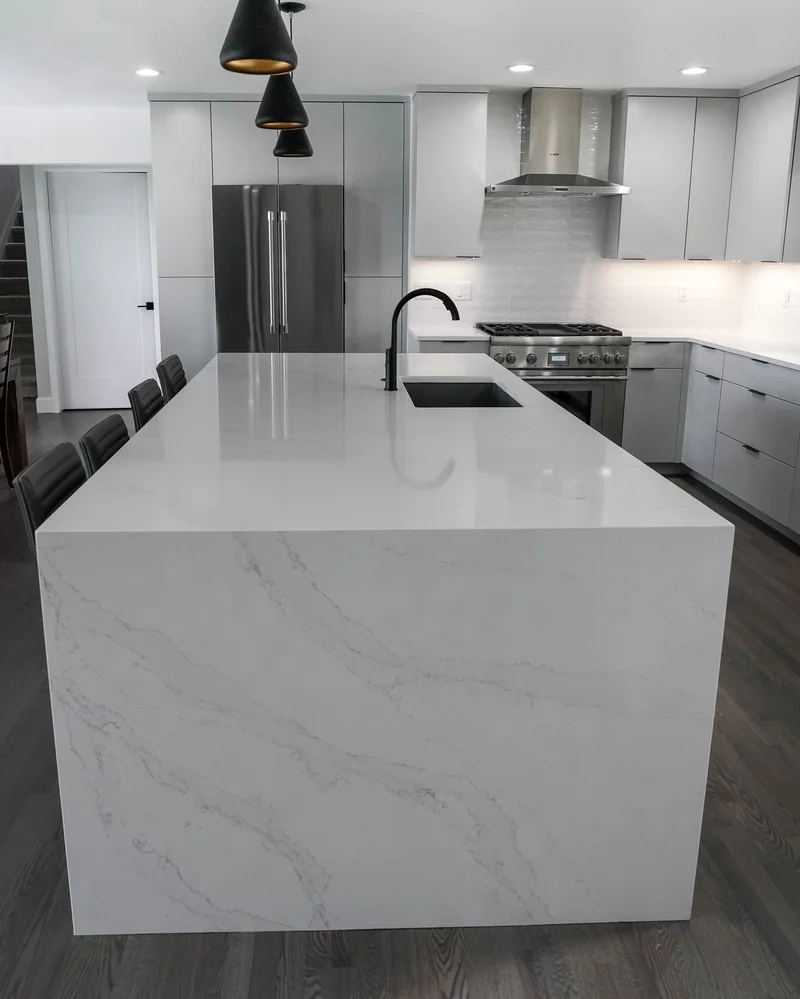 Waterfall quartz island end with a grey kitchen behind it