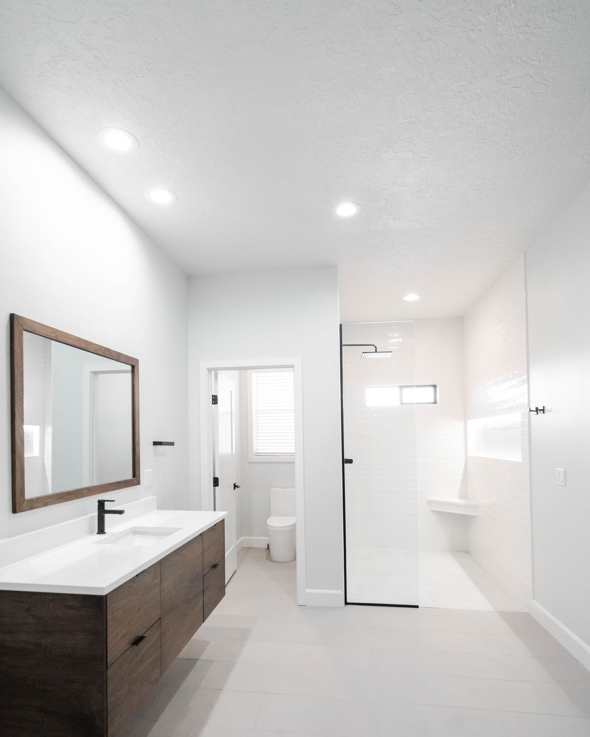 Bright white bathroom remodel with a walk-in shower, black fixtures, and floating walnut vanity