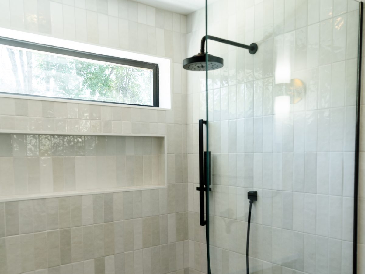 Curbless shower with vertical stacked tile, a black rain head, handheld, and a window over the niche