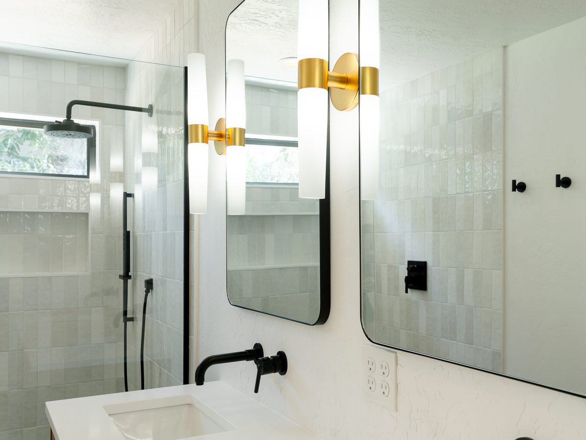 Angled view of the walnut vanity with brass sconces and the shower beyond