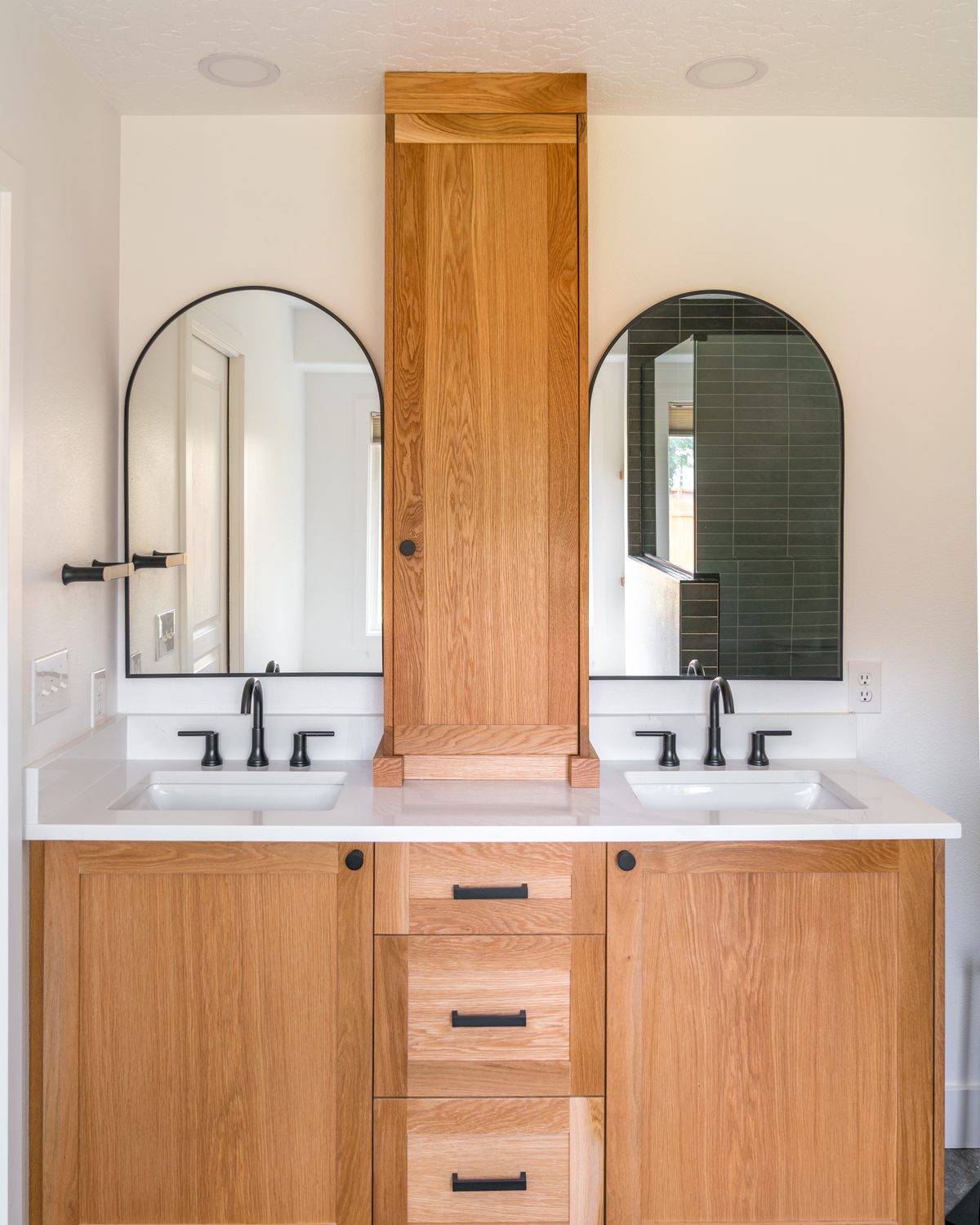 White oak double vanity with a storage tower and arched mirrors