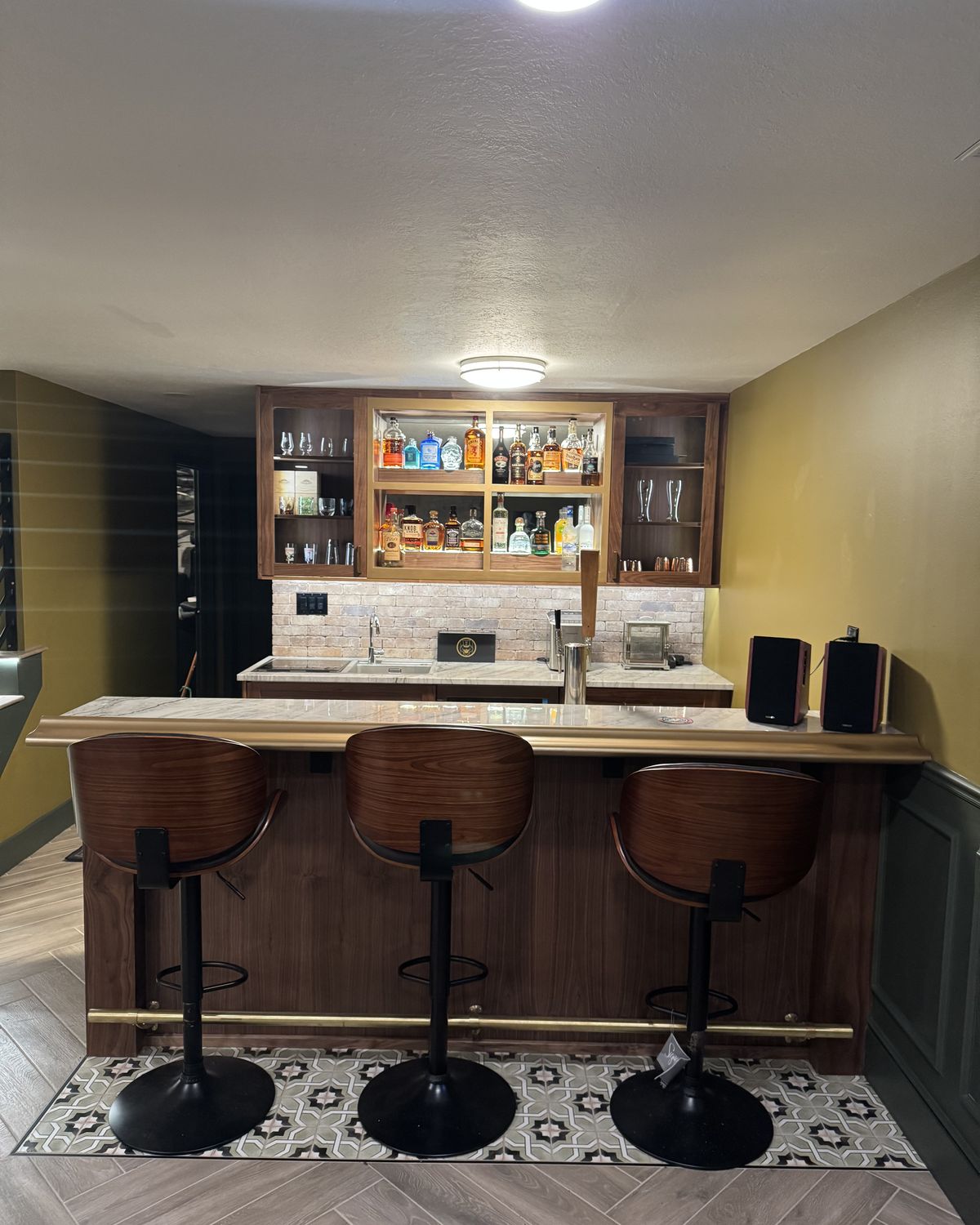Basement bar with walnut cabinets, a white stone counter, brass foot rail, and backlit liquor shelving