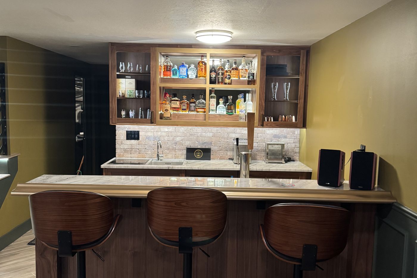 Basement bar with walnut cabinets, brass foot rail, and backlit shelving