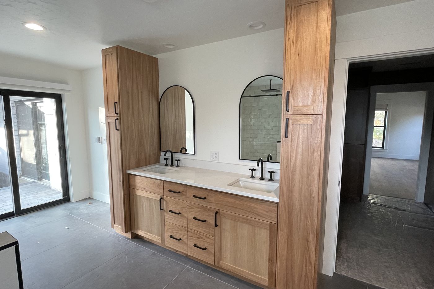 White oak double vanity with linen towers, black arched mirrors, and black wall-mount faucets