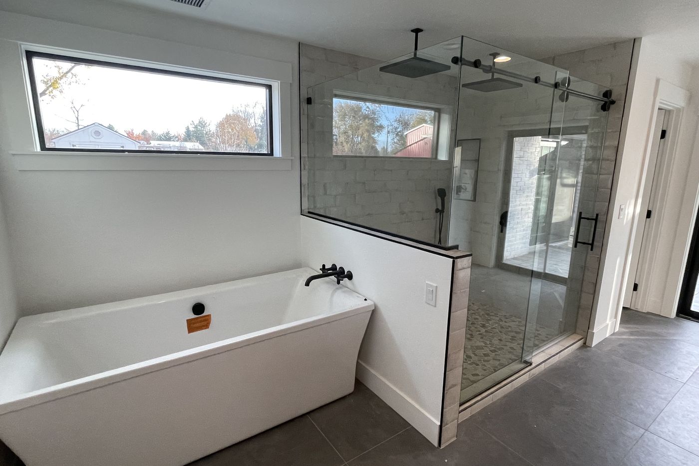 Master bath with a freestanding tub, black wall-mount filler, and a glass shower with two black rain heads