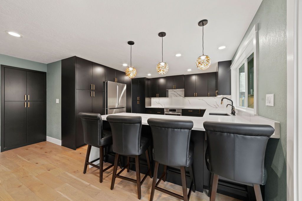 Black flat-panel kitchen with a quartz peninsula and gold pendants