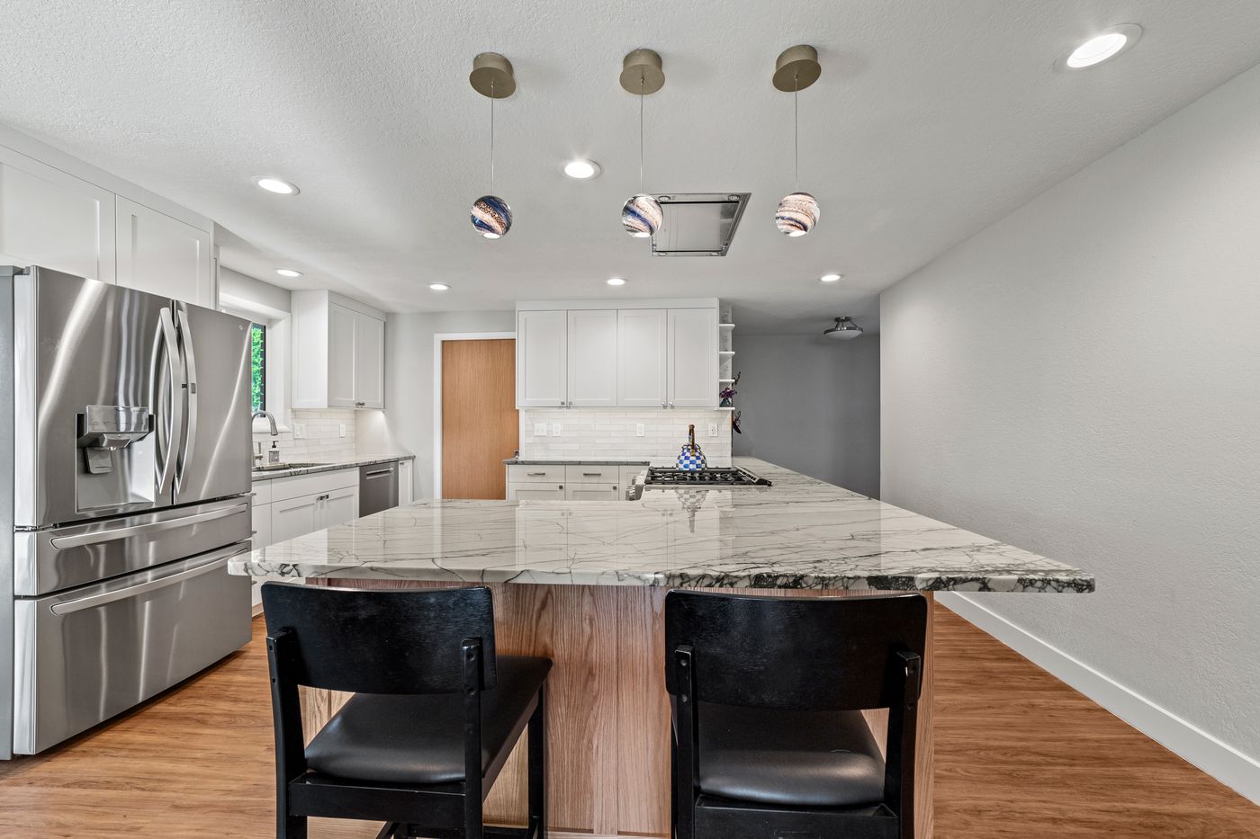 White shaker kitchen peninsula with bar stools and glass pendants