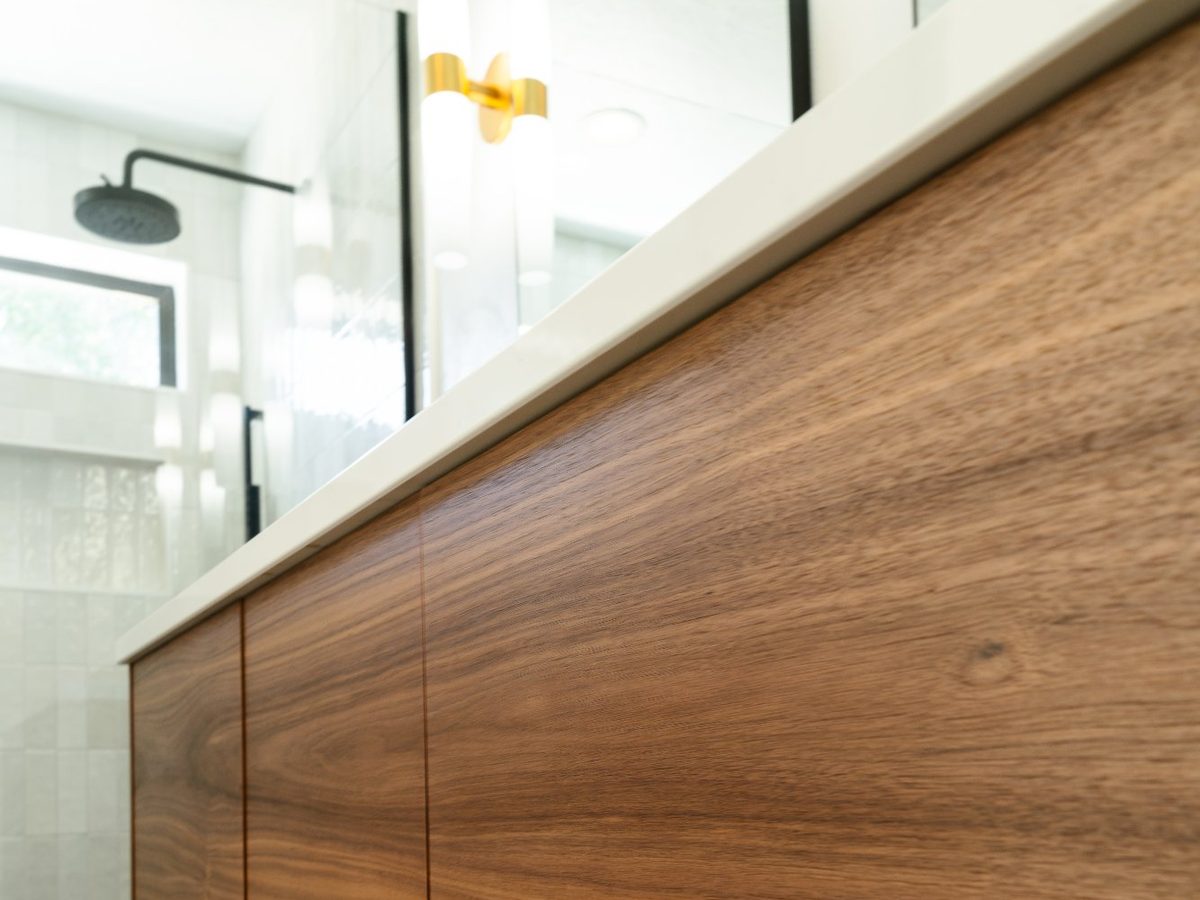 Grain-matched walnut vanity doors with a white quartz top, black rain head shower, and brass sconce behind